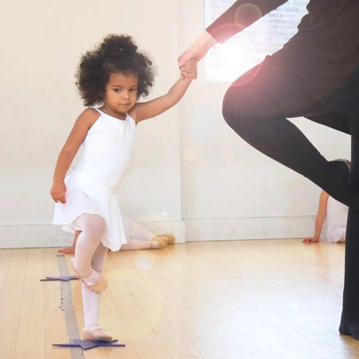 ballet dancer doing a passé while holding their grown up's hand in dance class