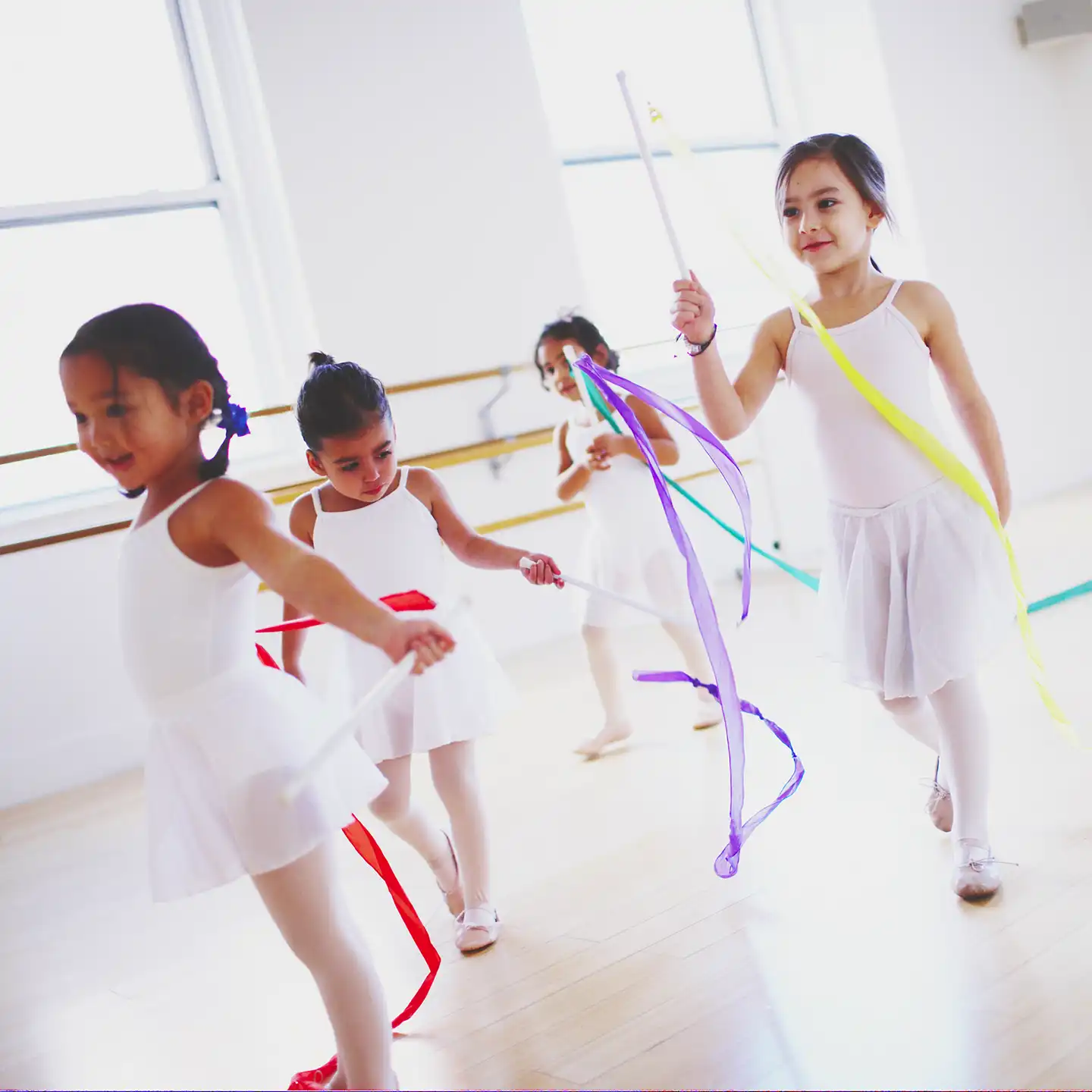 Preschoolers in white leotards dancing with ribbons.