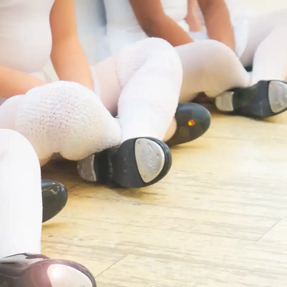 dancers wearing tap shoes sitting cross legged in a dance class