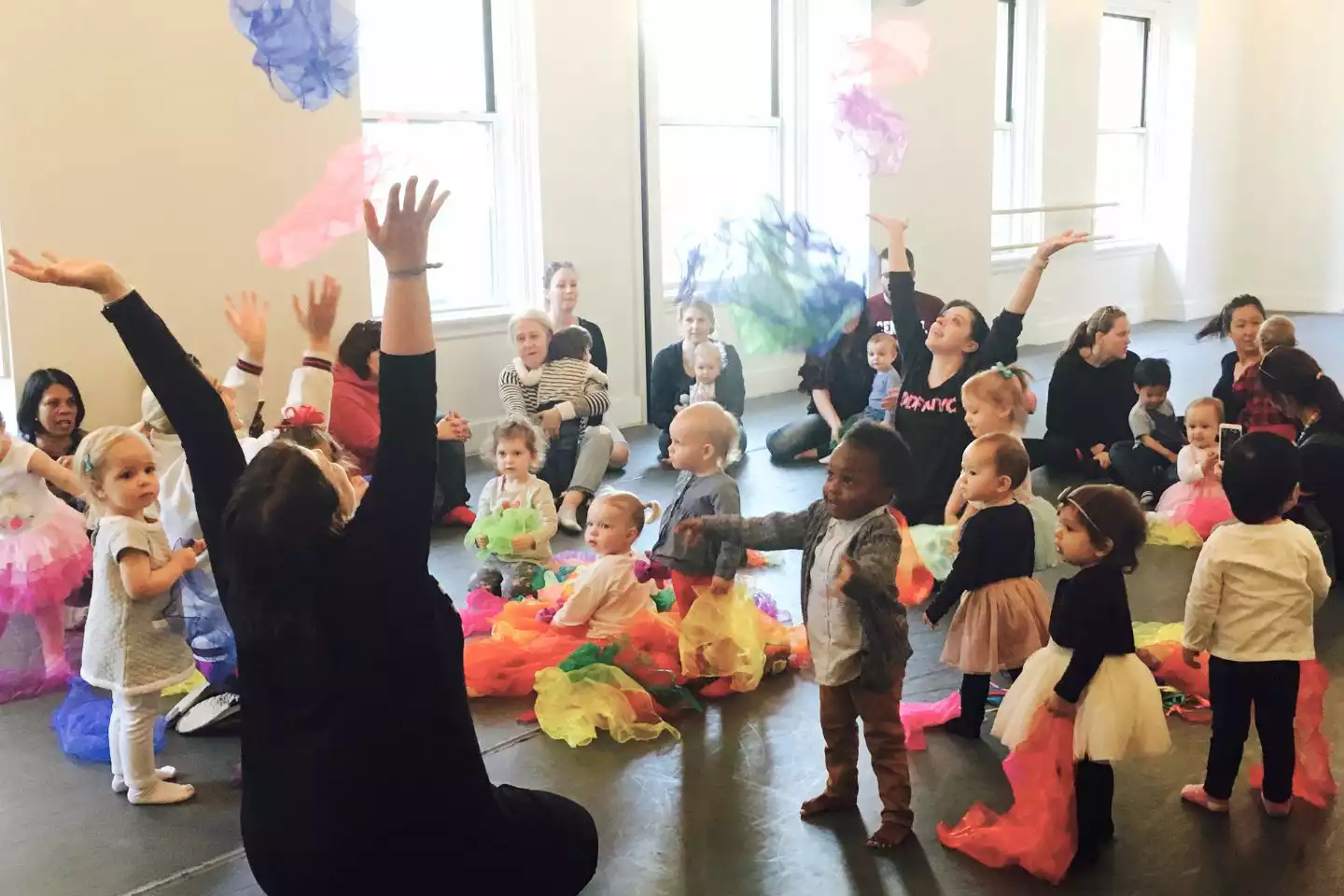 A group of toddlers and their parents and caregivers throwing colorful scarves in the air